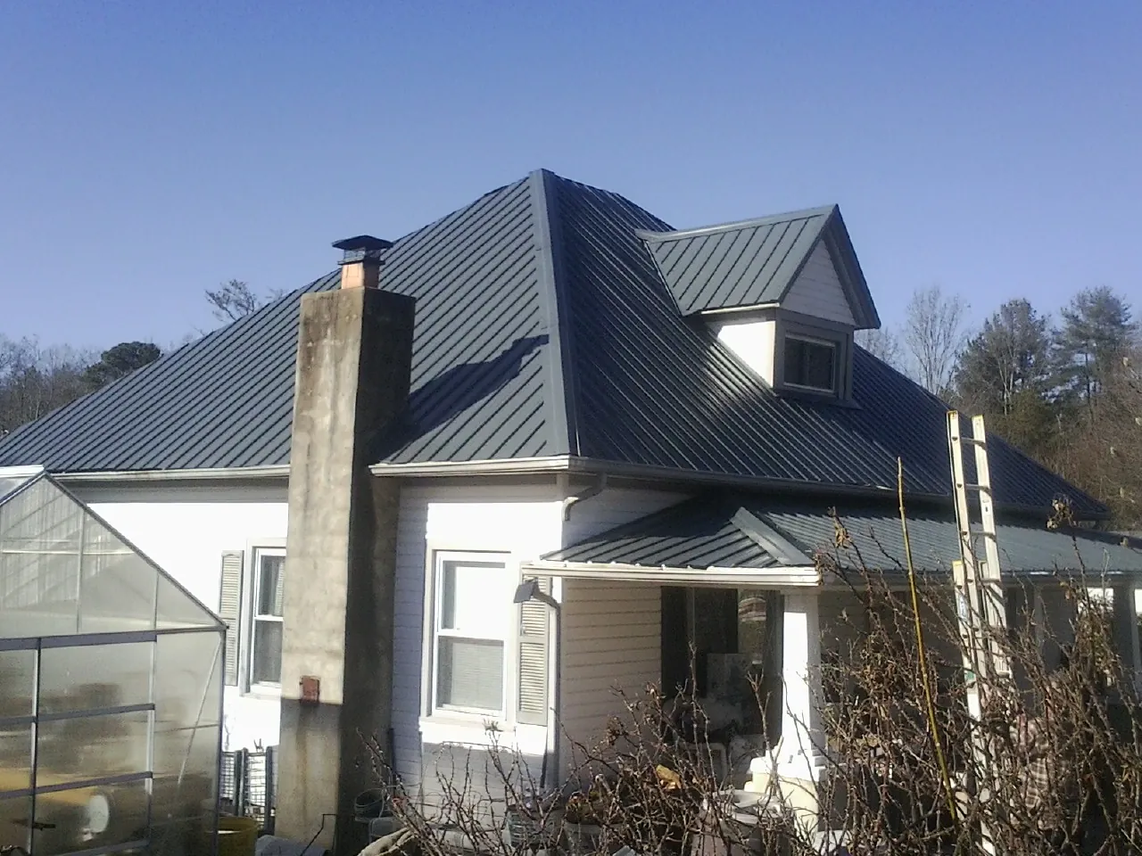 Dark blue standing seam metal roof on a white farmhouse with dormer — Slate & Tile Roof Repair by Roofing Brothers in Post