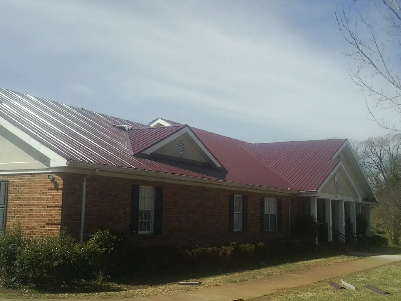 Red metal roof with gabled entries on a long brick building, from a Hail Damage Roof Repair job in Post