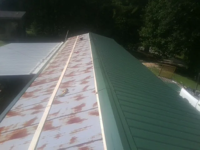 Old rusted panels beside newly installed green metal roofing — Wind Damage Roof Repair by Roofing Brothers in Post