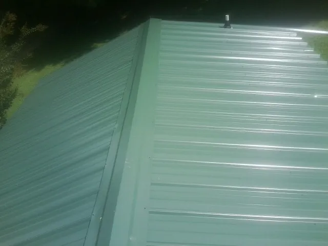 New green metal panels meeting at the ridge of a roof — Flat Roof Repair work by our crew in Post