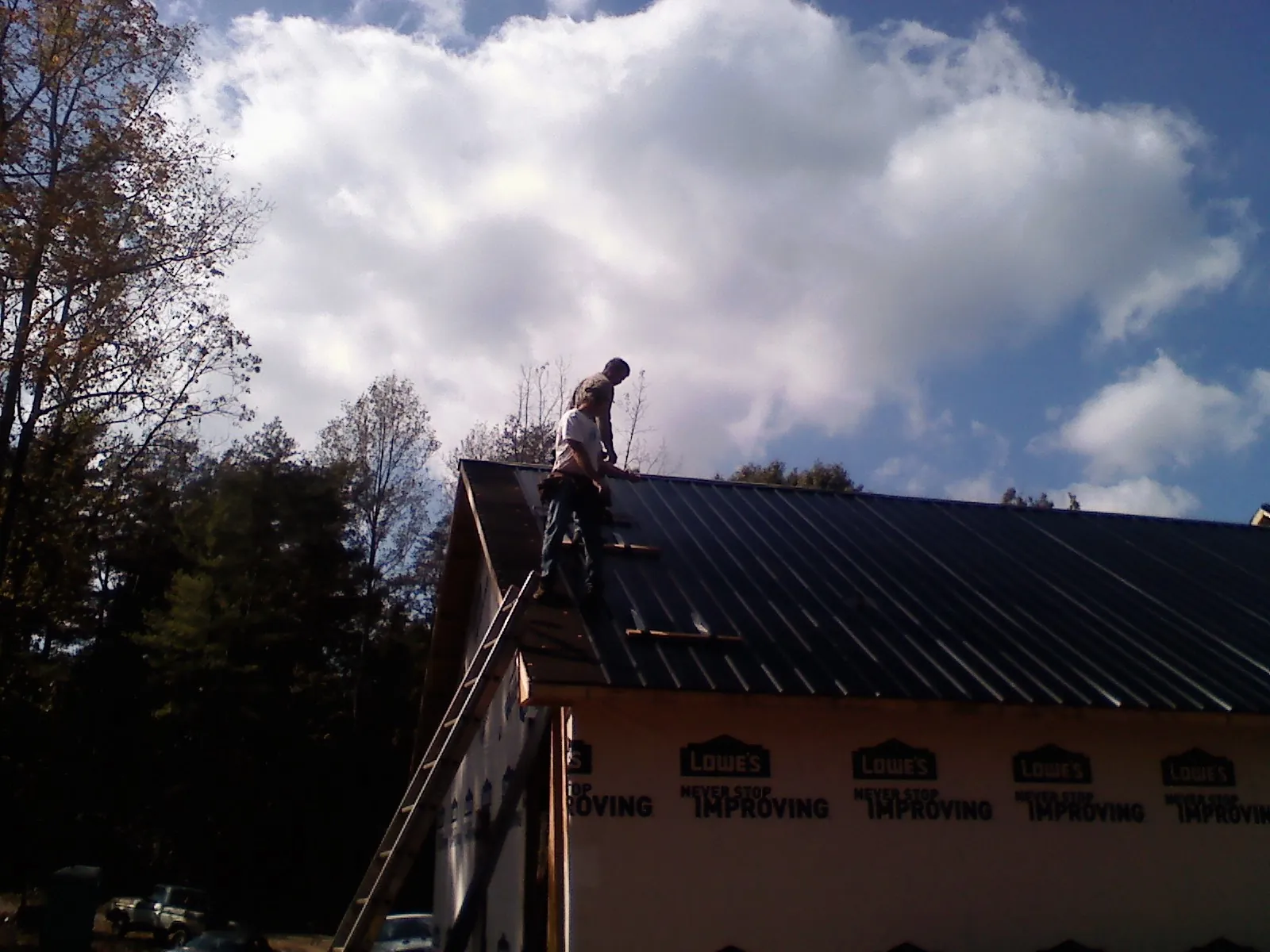 Roofer fastening dark metal panels high against a cloudy sky, from a Roof Inspection job in Post