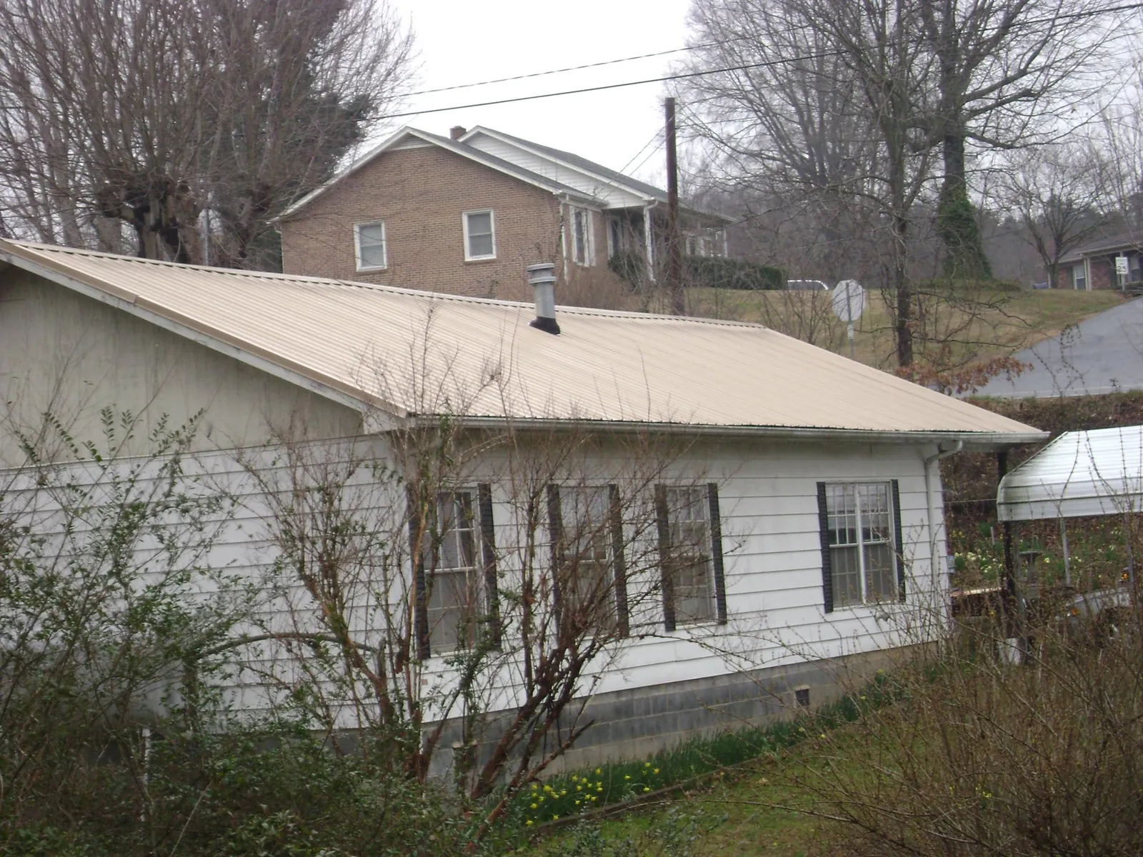 Tan metal roof on a white sided house set into a hillside — Commercial Roofing by Roofing Brothers in Post